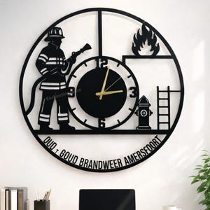 Puede incluir: Reloj de pared de metal negro con silueta de bombero, fuego e hidrante. Agujas doradas. Texto "OUD + GOUD BRANDWEER AMERSFOORT" en la parte inferior. El reloj está en una pared blanca. Diámetro aproximado de 40 cm.