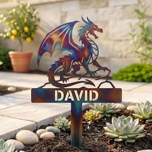 May include: A metal garden stake featuring a cutout dragon silhouette with a heat-treated iridescent finish. Below the dragon, a rectangular nameplate displays the name DAVID in bold, cut-out capital letters, supported by a vertical stake.