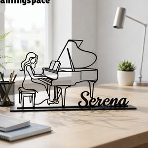 May include: Black metal piano silhouette with a woman playing, and the name "Serena" in cursive. The piano is on a desk with a plant, pencils, and notebooks. The word "Enchantingspace" is in the top left corner.