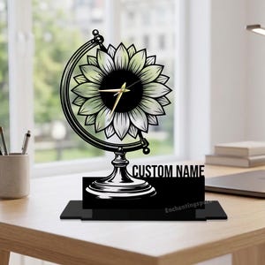 May include: A black and silver globe-shaped clock with a sunflower design. The clock has gold hands and the words "CUSTOM NAME" are printed on the base. The clock is on a wooden desk with a lamp and a laptop.