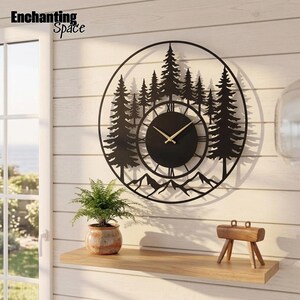 May include: A circular black metal wall clock featuring a silhouette of a pine forest and mountain range. The clock face is centered within the design, displaying Roman numerals and thin gold-colored hands. The text Enchanting Space is visible.