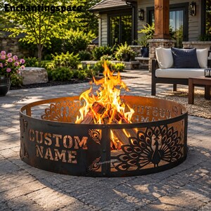 May include: A circular metal fire pit with a dark, weathered finish featuring cut-out designs of peacocks with fanned tails and the text CUSTOM NAME. Bright orange and yellow flames rise from the center, burning wood logs inside the structure.