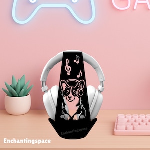 May include: A black headphone stand featuring a corgi wearing headphones, with musical notes above. The stand holds white headphones. The text "Enchantingspace" is at the bottom of the stand. The background is pink.