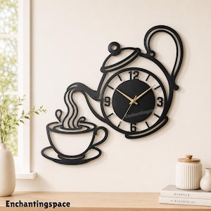 May include: A black wall clock shaped like a teapot pouring liquid into a teacup. The clock face is circular with gold-coloured hands and black numbers 3, 6, 9, and 12. The design features a continuous outline of a teapot, a stream of liquid, and a cup.