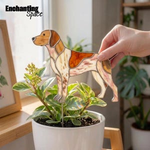 Può includere: Un ornamento per cani in vetro colorato con un mantello marrone e bianco a macchie, costruito con linee di metallo saldate. La figura del cane è fissata a un sottile paletto di metallo, progettato per essere inserito in un vaso di piante.