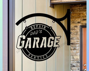 May include: A circular black metal hanging sign with a decorative bracket. The sign features white text that reads "REPAIR DAD'S GARAGE SERVICE" in a bold, stylized font. The sign is suspended by two silver-colored metal chains from the bracket.