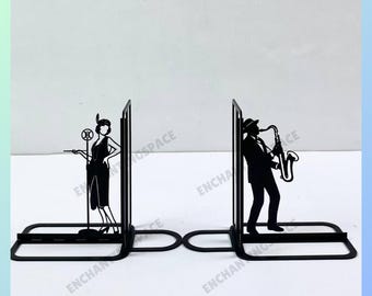Puede incluir: Dos sujetalibros de metal negro con la silueta de una mujer con un micrófono y un hombre tocando el saxofón. Los sujetalibros están conectados por una barra de metal.