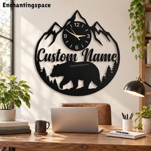 Può includere: Un orologio da parete circolare nero con una silhouette di catena montuosa in alto, un orso che cammina attraverso una foresta in basso e il testo Custom Name in carattere corsivo. Il quadrante ha lancette dorate e numeri bianchi 3, 6, 9 e 12.