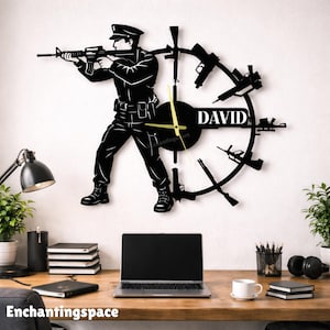 May include: Black metal wall clock featuring a silhouette of a person aiming a rifle, surrounded by gun designs. The clock face includes the name "DAVID" and the text "Enchantingspace". The clock hands are gold.