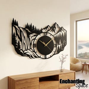 May include: A black metal wall clock featuring a laser-cut silhouette of a mountain range, a waterfall, and pine trees. The circular clock face has gold-colored hands and numbers at the 3, 6, 9, and 12 positions, integrated into the landscape design.