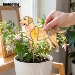 May include: A stained glass Labrador retriever dog figure in shades of yellow and cream with a pink tongue, attached to a thin metal stake. The dog is positioned upright, featuring distinct glass segments outlined in dark metal solder.