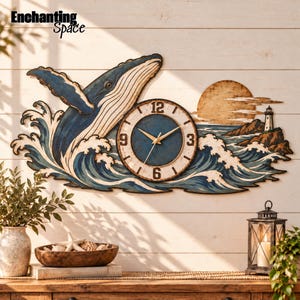 Könnte beinhalten: Eine Wanduhr mit einem aus Meereswellen springenden Blauwal, einer goldenen Sonne und einem Leuchtturm an einer Felsküste. Das Zifferblatt hat eine dunkelblaue Mitte, einen weißen Rand mit schwarzen Zahlen und goldene Zeiger. Der Text Enchanting Space ist sichtbar.
