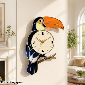 May include: A stained glass wall clock shaped like a toucan with a large orange beak, a cream-colored face, and dark blue and black body feathers. The clock face is circular with black numerals at 3, 6, 9, and 12, and gold-colored hands.