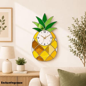 May include: A pineapple-shaped wall clock featuring stained glass panels in shades of yellow and orange for the body and green for the leaves. The centre has a white circular clock face with black numerals and gold-toned hands.