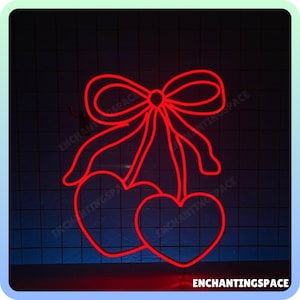 May include: Red neon sign shaped like two cherries with a bow on top. The sign is lit up and glowing against a dark background.