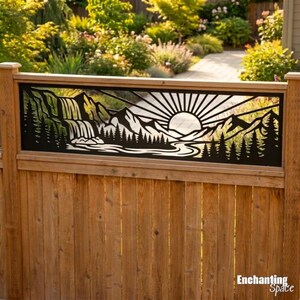 May include: A black metal fence panel featuring a laser-cut landscape design of a sunburst over mountain peaks, a flowing river, and a forest of pine trees. The panel is mounted horizontally onto a vertical wooden fence structure.