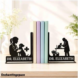 Może przedstawiać: Para czarnych metalowych podpórek do książek z sylwetkami weterynarza z psem i weterynarza z kotem. Każdy element zawiera napis DR. ELIZABETH oraz symbol krzyża medycznego, podtrzymując cztery książki ustawione pionowo między nimi.