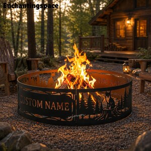 May include: A circular black metal fire pit ring featuring laser-cut silhouettes of pine trees and a fox sitting on a tree stump. The metal panels include a rectangular cutout with the text CUSTOM NAME, surrounding a bright orange wood fire.