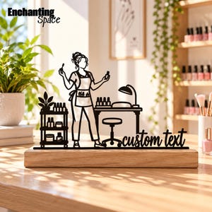Könnte beinhalten: Eine schwarze Metallsilhouette einer Nageldesignerin an einem Arbeitsplatz mit Rollwagen, Schreibtisch, Lampe und Hocker, montiert auf einem rechteckigen Holzsockel. Das Design enthält den Text custom text und Enchanting Space.