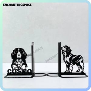 Op de afbeelding: Zwarte metalen boekenleggers met een silhouet van een hond aan elke kant. De boekenlegger aan de linkerkant heeft het woord "COSMO" op de basis gedrukt.