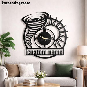 Könnte beinhalten: Eine schwarze Wanduhr mit einem ausgeschnittenen Design aus einem Tornado und einer Sonne. Das runde Zifferblatt hat goldene Zeiger sowie die Zahlen 3, 6, 9 und 12. Unter dem Zifferblatt befindet sich ein Banner mit dem Text custom name.