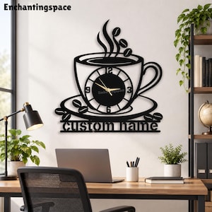 May include: A black wall clock shaped like a coffee cup on a saucer with steam and coffee beans above. The clock face features gold hands and numbers 3, 6, 9, and 12. Below the saucer, the text custom name is displayed in a bold black font.