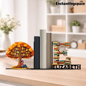 May include: A decorative bookshelf with a tree design, a stack of books, and the name "ELIZABETH". The tree has an autumn color scheme, and a person is sitting under it reading. The letter "E" is made of books.