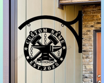 May include: A black circular metal sign featuring a central anvil and two crossed hammers. The text CUSTOM NAME is arched at the top, and EST. 2025 is at the bottom. The design includes chain links and stars, suspended from a curved metal bracket.