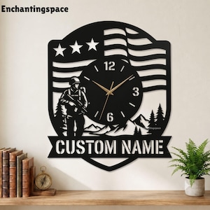 May include: A black wall clock featuring a silhouette of a soldier holding a rifle, a stylised American flag, and a mountain landscape. The clock face has gold-coloured hands and numbers. A banner at the bottom displays the text CUSTOM NAME.