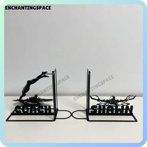 Puede incluir: Un par de sujetalibros de metal negro con la silueta de un buceador. Los sujetalibros están etiquetados como "Coach" y "Shawn".