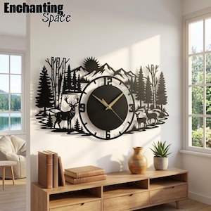 May include: A black metal wall clock featuring a laser-cut silhouette of a mountain landscape with pine trees, a sun, and two deer. The circular clock face has gold-colored hands and the numbers 3, 6, 9, and 12 in a bold, sans-serif font.