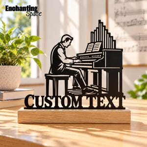 May include: A black metal silhouette sculpture depicting a person playing a pipe organ, mounted on a rectangular light-colored wooden base. The design features the words CUSTOM TEXT in bold capital letters at the bottom of the metal cutout.
