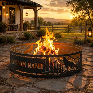 May include: A circular black metal fire pit ring featuring laser-cut silhouettes of pine trees, mountains, and wolves. The side of the ring displays the text CUSTOM NAME in bold capital letters. A bright orange fire burns inside the metal ring.
