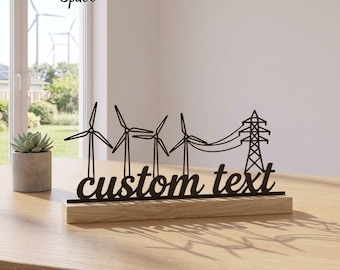 Op de afbeelding: Een zwart metalen silhouetbord met drie windturbines en een elektriciteitsmast, gemonteerd op een rechthoekige lichte houten voet. Het bord toont onderaan de woorden custom text in een cursief lettertype.