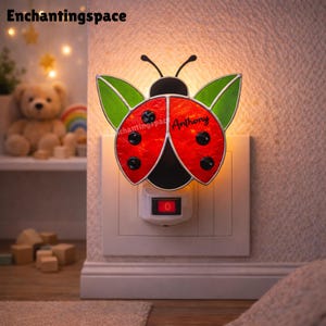 May include: A ladybug-shaped night light with a red body, black spots, and green wings. The night light is plugged into a wall outlet and has a small on/off switch. The name "Anthony" is written on the ladybug. The brand name "Enchantingspace" is at the top.