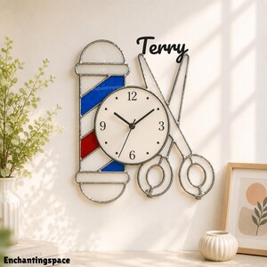 May include: A decorative wall clock featuring a barber pole design, a clock face, and large scissors. The clock face has black hands and numbers. The name "Terry" is written above the scissors. The barber pole has red, white, and blue stripes.