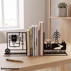 May include: A pair of black metal bookends featuring an electronic circuit diagram with an integrated circuit, resistor, and capacitor on one side, and an electrical transmission tower with the text ALEXANDER SMITH on the other side.