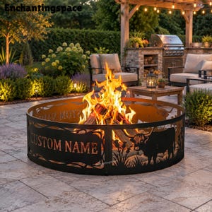 May include: A circular black metal fire pit ring featuring cut-out silhouettes of Highland cattle and grass, with a rectangular panel displaying the text CUSTOM NAME. A bright orange and yellow fire burns inside the metal structure.