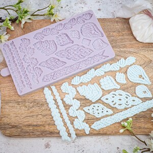 May include: A purple silicone mold with a variety of lace-like designs, including leaves, flowers, and borders. The mold is on a wooden cutting board with a light blue icing design that has been made using the mold.