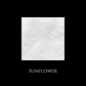 May include: White paper napkin with an embossed sunflower design. The napkin has a raised, textured pattern of a sunflower with leaves and smaller flowers.