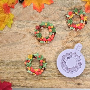 May include: Three autumn-themed wreaths made with polymer clay, featuring mushrooms, leaves, and berries. A purple silicone mold for making wreaths is also shown.