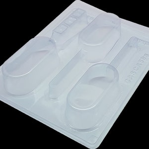 May include: Clear plastic mould with four cavities for making chocolate or sweets. The mould has two oval shapes and two long, thin rectangular shapes. The mould is labelled "GASCANA" on the side.
