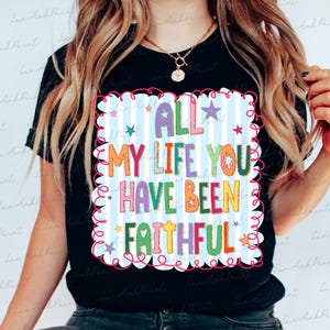 May include: Black t-shirt with a colorful graphic that reads "ALL MY LIFE YOU HAVE BEEN FAITHFUL." The design features a light blue striped background, stars, and a decorative border. The text is in various bright colors.