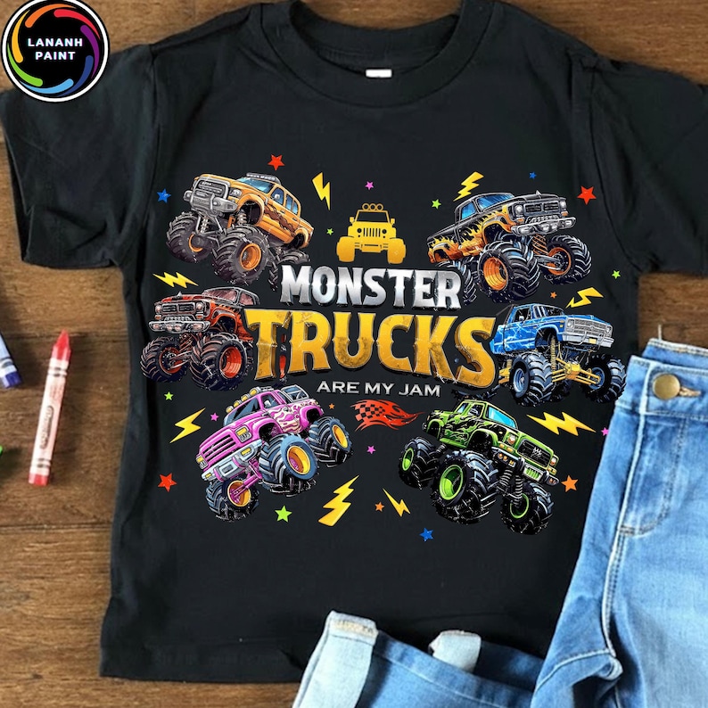 K&ouml;nnte beinhalten: Schwarzes T-Shirt mit einer farbenfrohen Grafik von Monstertrucks. Das Design zeigt verschiedene Monstertrucks in verschiedenen Farben, Blitze und den Text "MONSTER TRUCKS ARE MY JAM". Das Shirt wird mit blauen Jeans kombiniert.