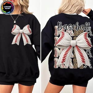 Könnte beinhalten: Schwarzes Sweatshirt mit einer großen, weißen Schleife mit roten Baseballnähten auf der Vorderseite. Auf der Rückseite des Sweatshirts steht das Wort "Baseball" und das Wort "Mama" mehrfach wiederholt, zusammen mit einer Schleife.