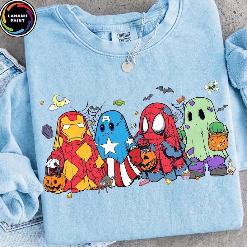 May include: A light blue crewneck sweatshirt featuring a graphic print of four cartoon characters dressed as ghosts for Halloween. The characters resemble Iron Man, Captain America, Spider-Man, and a green ghost, each holding a pumpkin candy bucket.
