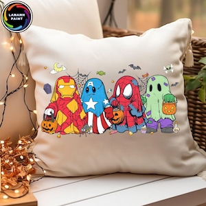 May include: A cream-colored square throw pillow featuring a graphic print of four characters dressed as ghosts for Halloween. The characters resemble Iron Man, Captain America, Spider-Man, and a green ghost, each holding a small orange pumpkin bucket.