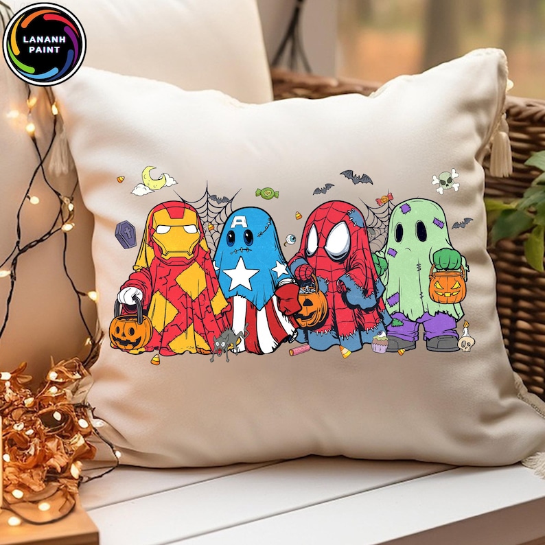 May include: A cream-colored square throw pillow featuring a graphic print of four characters dressed as ghosts for Halloween. The characters resemble Iron Man, Captain America, Spider-Man, and a green ghost, each holding a small orange pumpkin bucket.