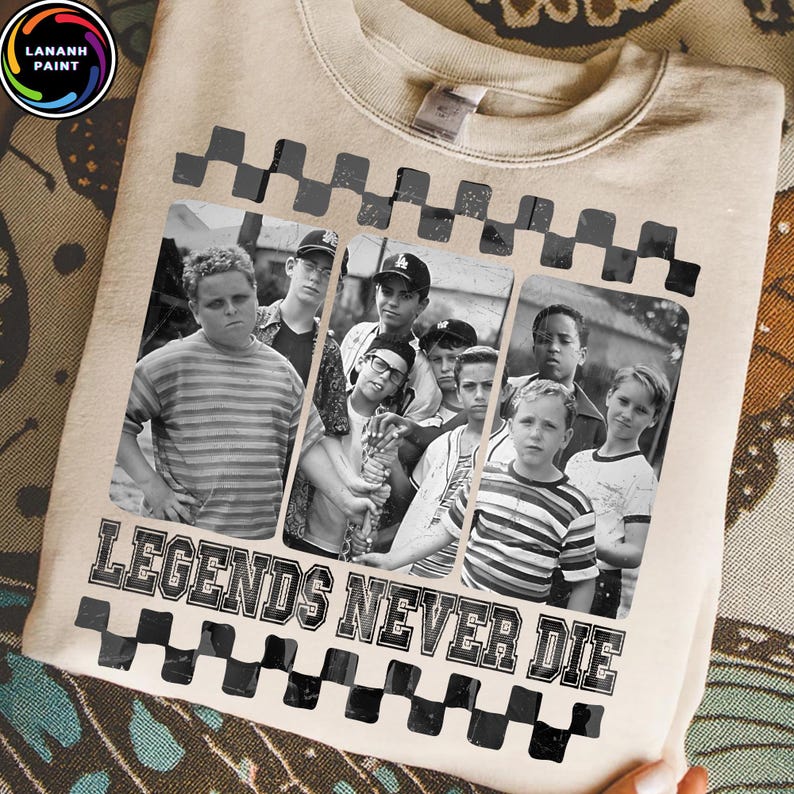 May include: Beige sweatshirt featuring a black and white image of a group of boys. The image is framed with a black and white checkered pattern. The text "LEGENDS NEVER DIE" is printed in black below the image.