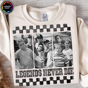 Puede incluir: Sudadera de color crema con una imagen en blanco y negro de un grupo de chicos. La imagen está enmarcada con un patrón de cuadros y las palabras "LEGENDS NEVER DIE" están impresas debajo en negrita.